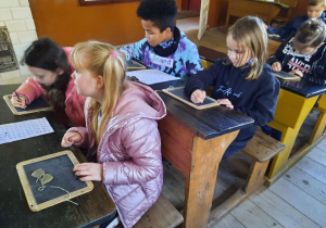 Uczniowie siedzą w starych ławkach i piszą