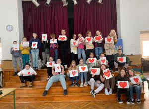 Uczniowie siedzą na schodach w auli i trzymają kartki z sercem