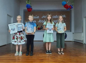 Czworo dzieci trzyma nagrody i dyplomy stojąc na scenie w auli.