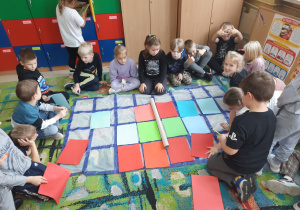 Uczniowie siedzą na podłodze przy macie do kodowania