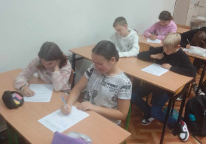 Uczniowie siedzą przy stolikach w klasie