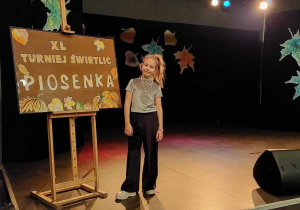 Dziewczynka stoi przy plakacie Turniej Świetlic - Piosenka