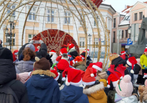 Tłum ludzi w czapkach Świętego Mikołaja stoi przed świecącą bombką z tronem.