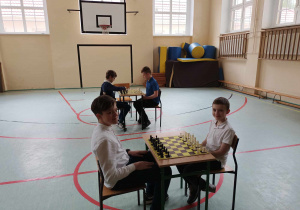 Uczniowie przy dwóch stołach grają w szachy.