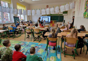 Grupa uczniów stoi i siedzi w klasie