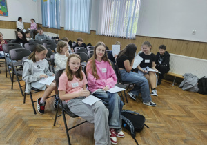 Uczniowie siedzą na krzesłach na auli podczas warsztatów.