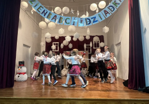 Uczniowie na scenie tańczą taniec ludowy.