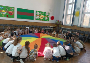 Wszystkie dzieci i nauczyciel siedzą przy chuście.