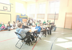 Uczniowie siedzą przy stolikach i biorą udział w konkursie.