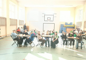 Uczniowie siedzą przy stolikach i biorą udział w konkursie.