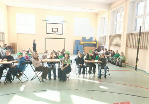 Uczniowie siedzą przy stolikach i biorą udział w konkursie.