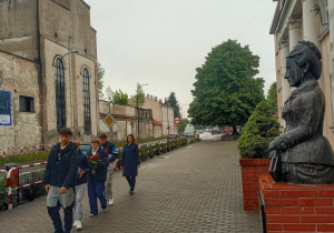 Delegacja uczniów idąca złożyć kwiaty i znicze przed popiersiem patronki.